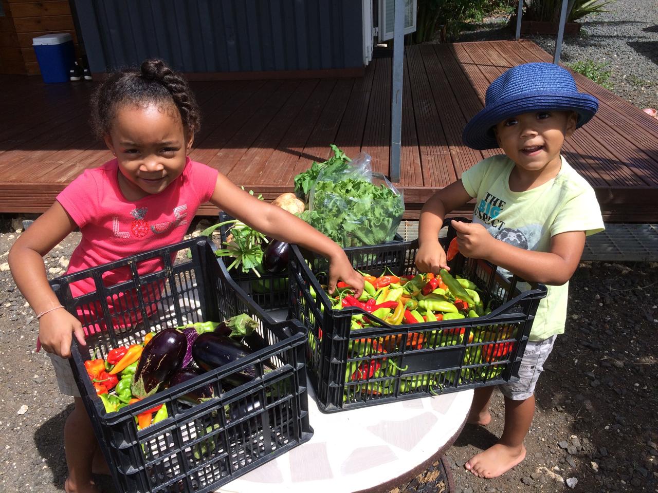 Deux enfants présentant fièrement des cagettes de piments et légumes fraîchement récoltés